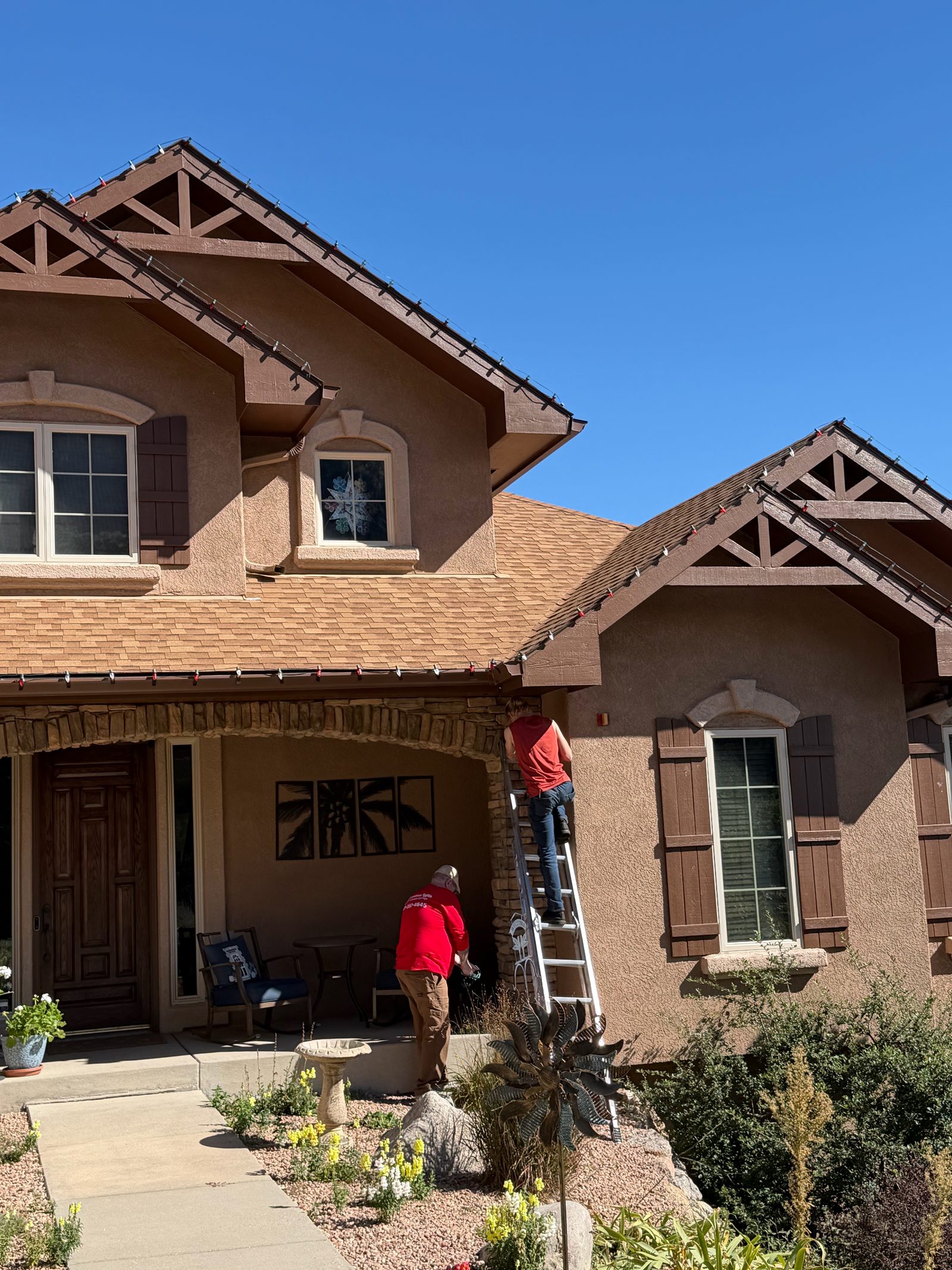 Our crew on ladder installing roofline Christmas lights by the front porch Our crew on ladder installing roofline Christmas lights by the front porch